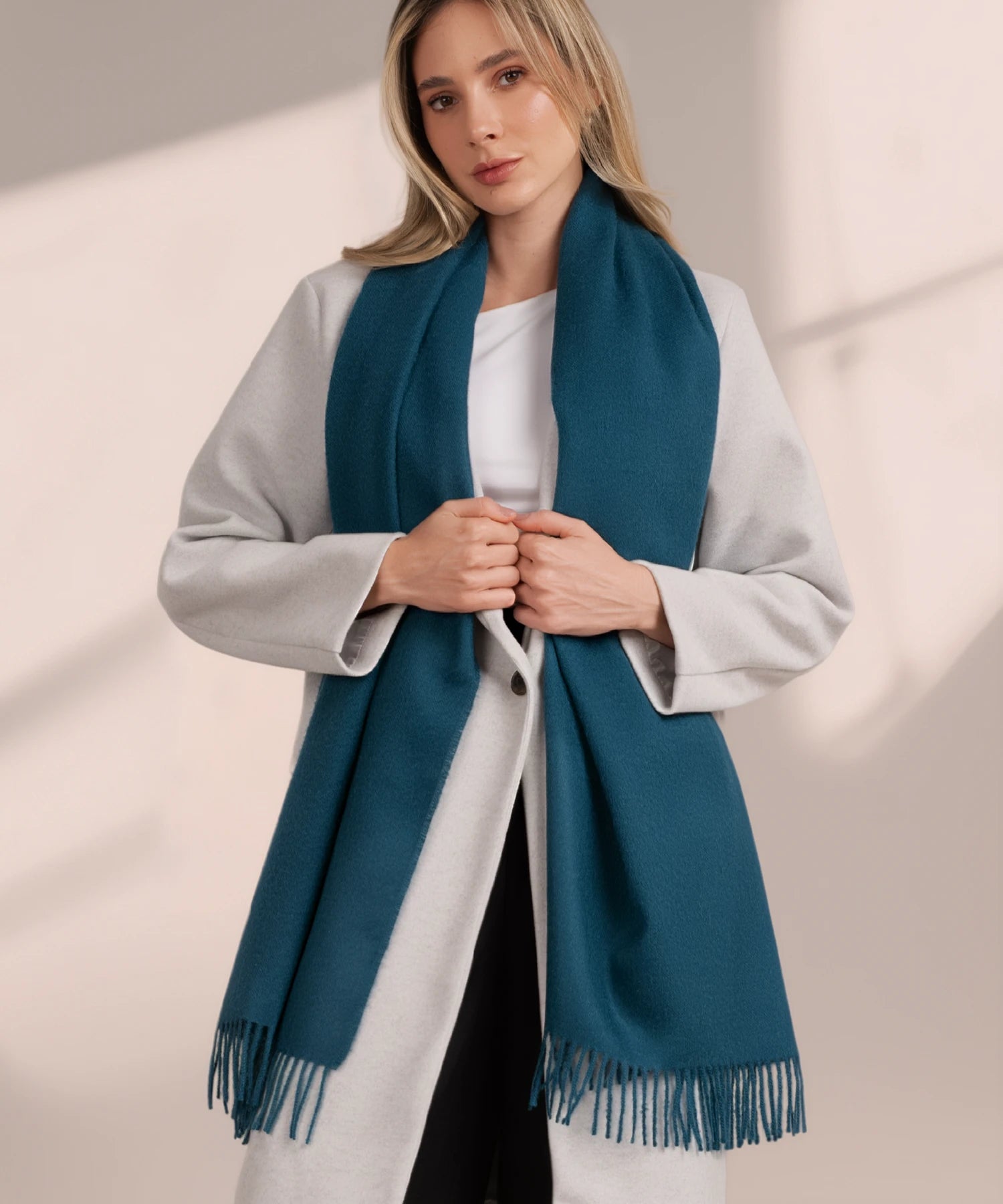Woman wearing a teal scarf over a light gray coat on a neutral background