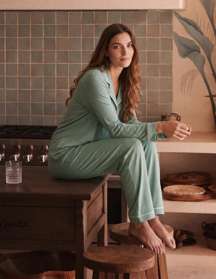 Woman in teal pajamas sitting on a kitchen counter holding a mug.