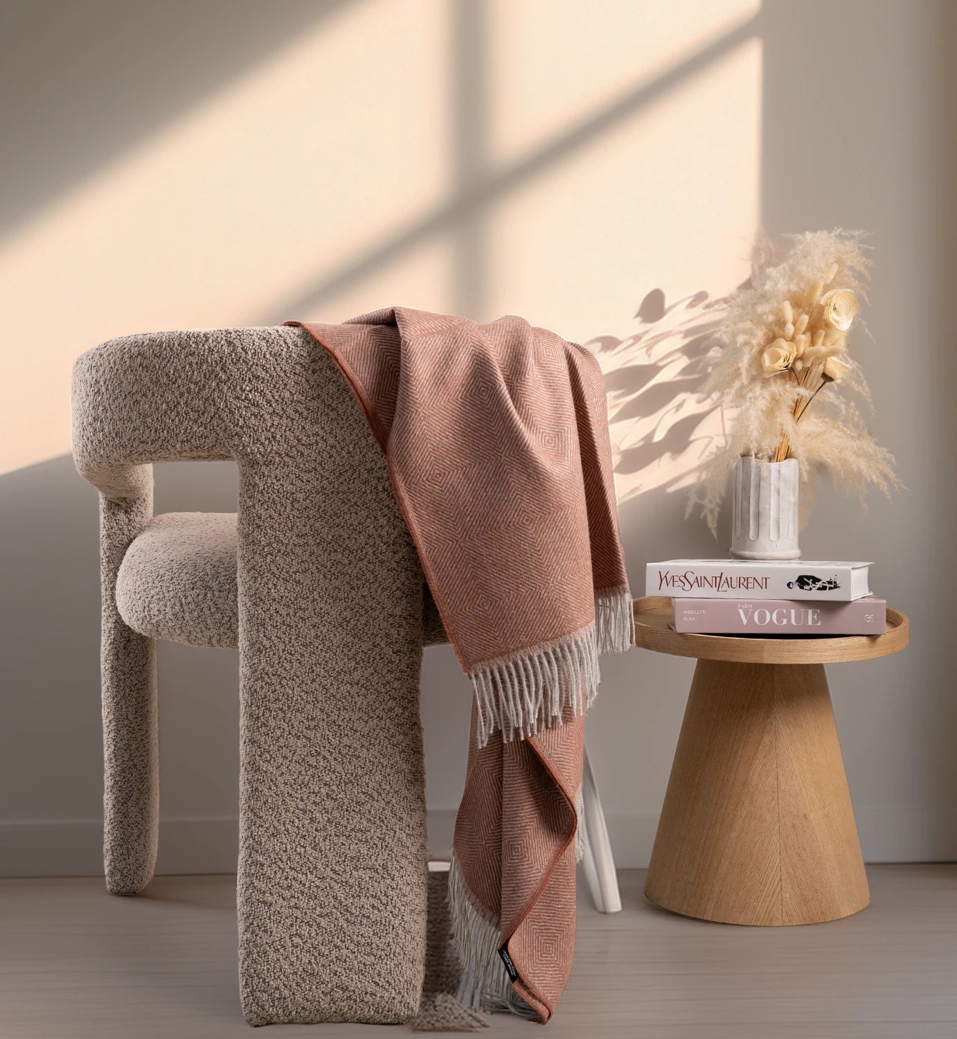 Beige textured chair with a pink blanket draped over it, next to a wooden side table with books and decor.