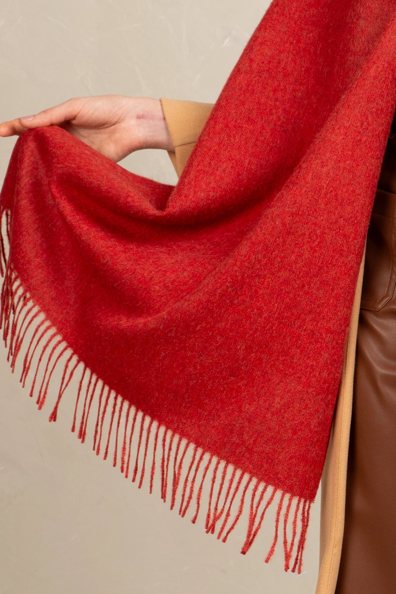 Red scarf with fringes draped over a person wearing a brown leather jacket.