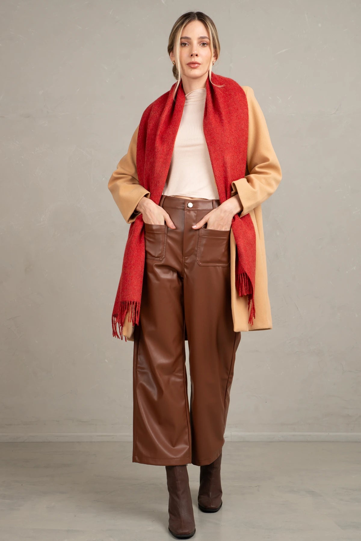 Woman wearing a beige coat, baby alpaca red scarf, and brown leather pants against a plain background