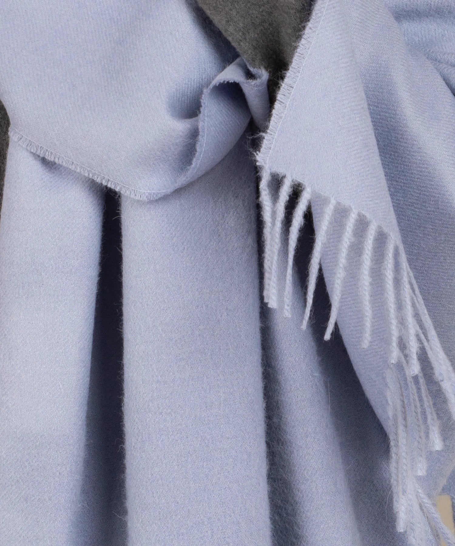 Close-up of a light blue scarf with fringes on a neutral background