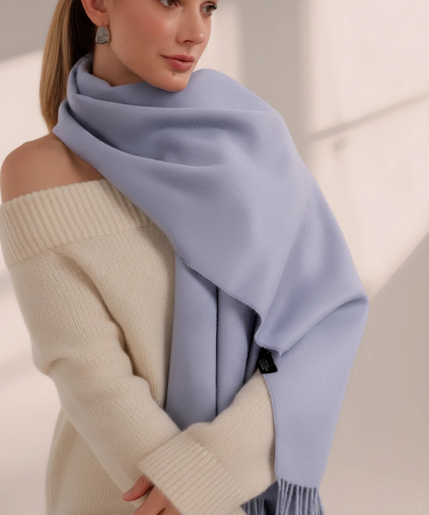 Woman wearing a light blue scarf and beige sweater against a neutral background