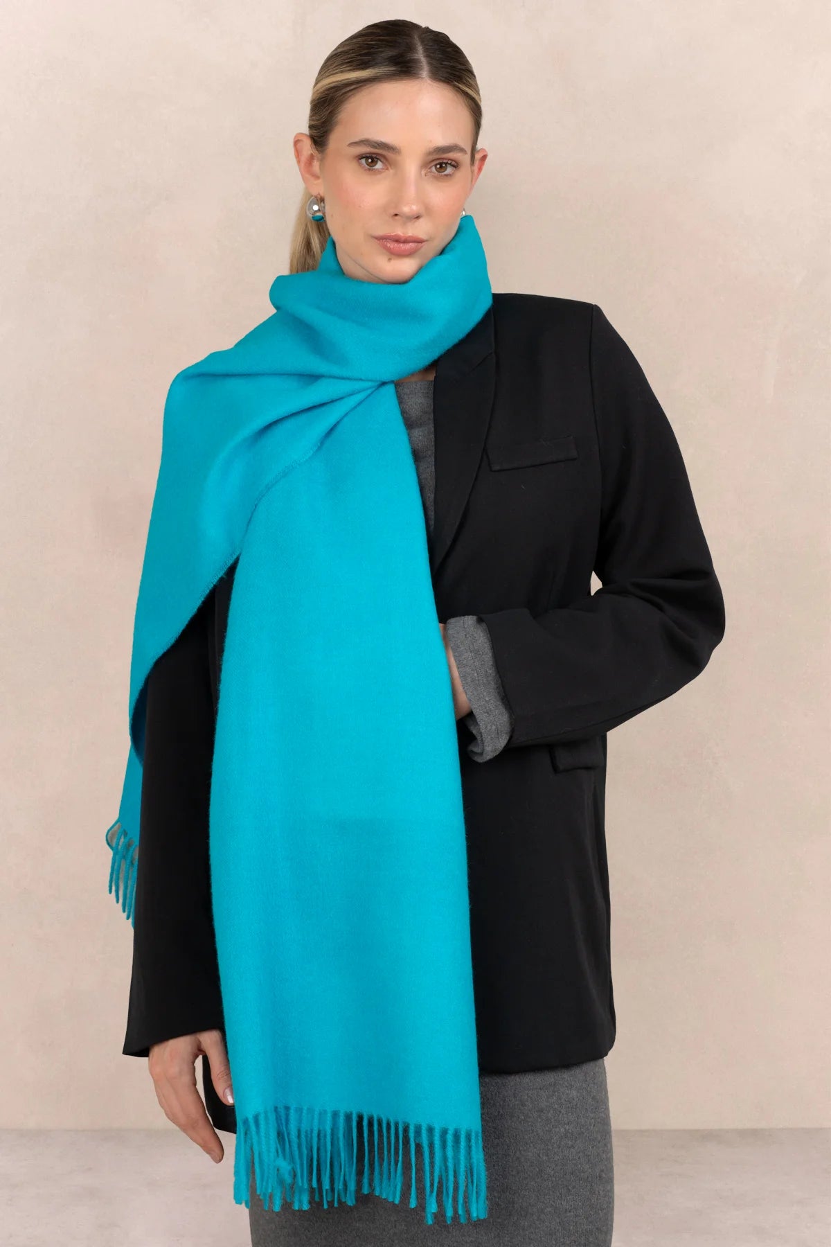 Woman wearing a turquoise scarf and black coat against a beige background