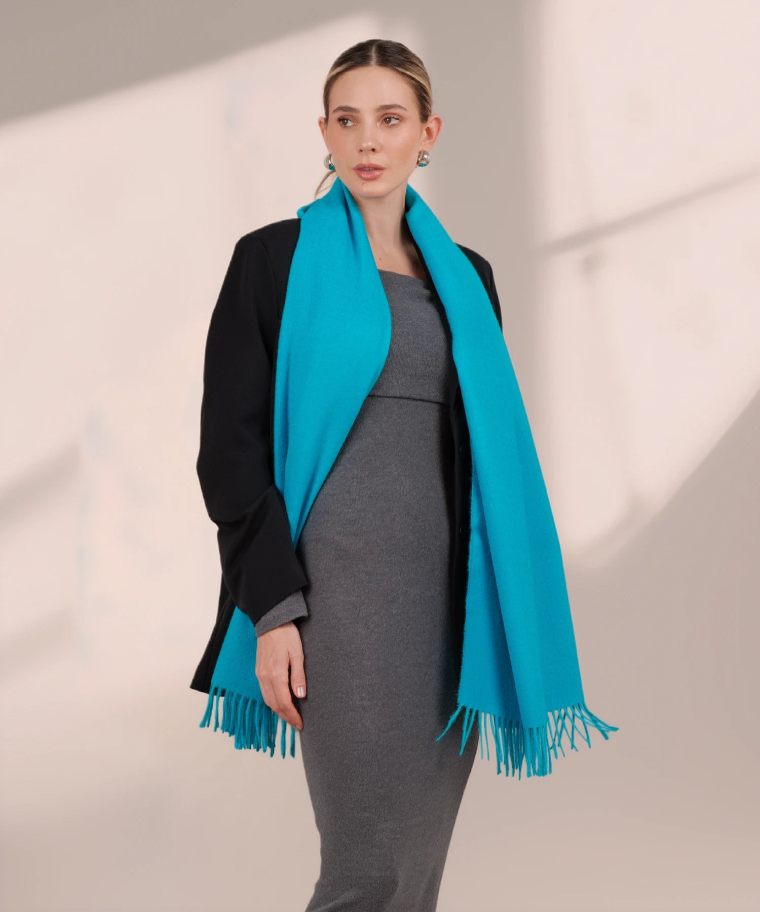Woman wearing a black coat with a bright blue scarf against a neutral background