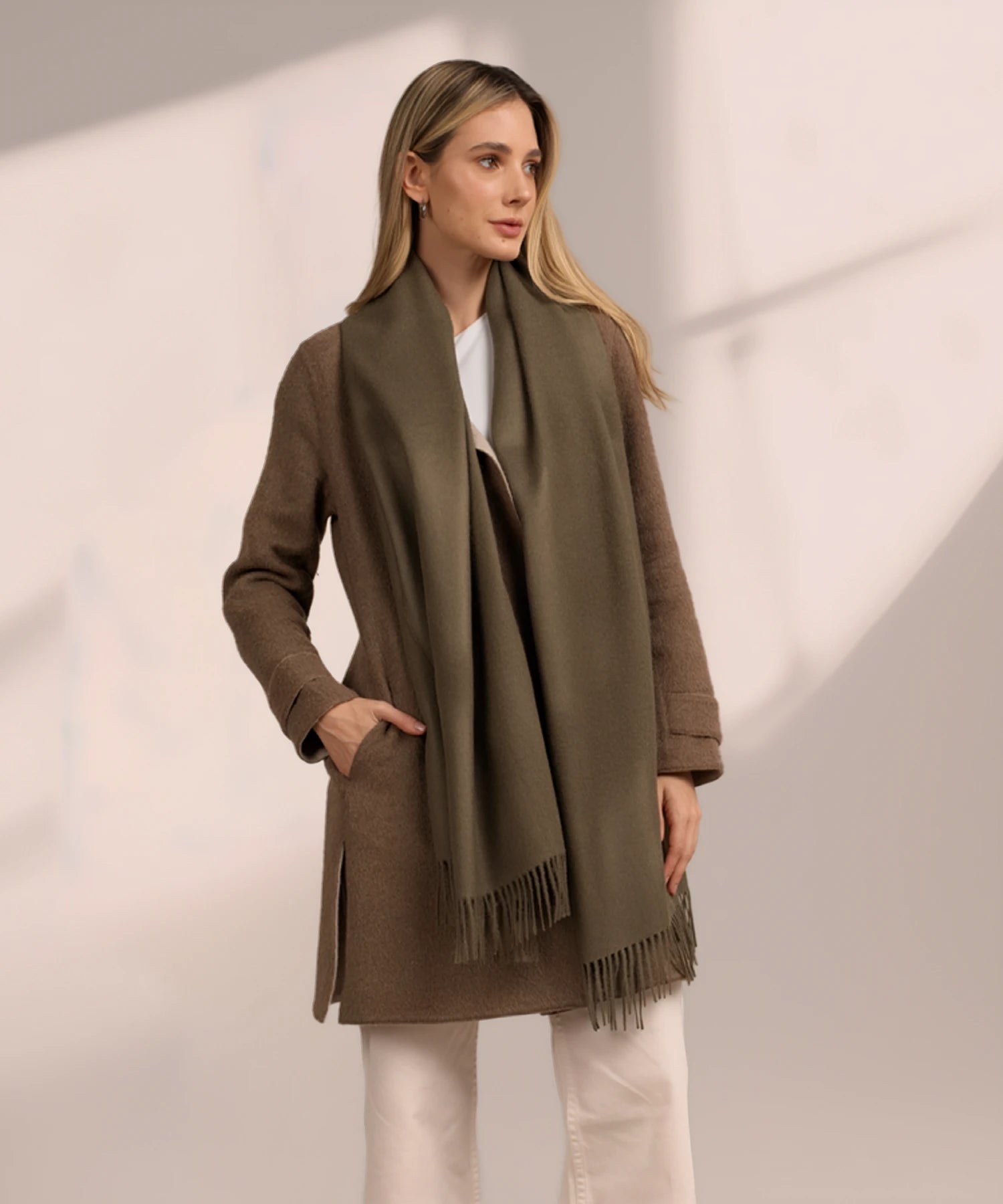 Woman wearing a brown coat and green scarf on a light background